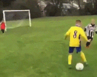 a young boy kicks a soccer ball toward a goal where the goalie is not paying attention, an adult labeled `!important` pushes the goalie down to the ground to block the ball